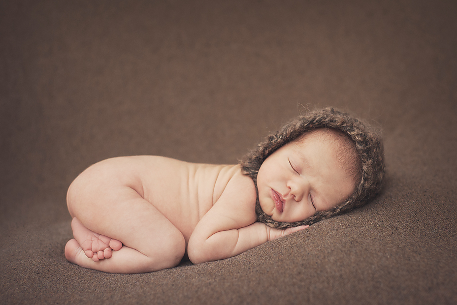 baby sleeping on brown blanket wearing a bonnet