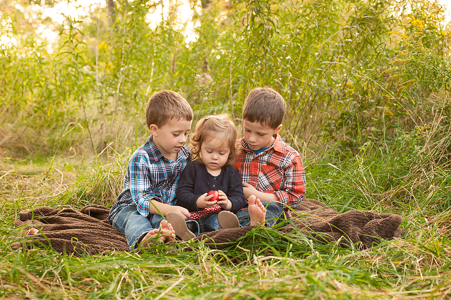 three children sitting together closely in the grass