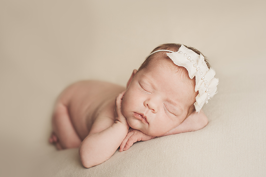 Newborn baby girl with headband and hand resting on cheek