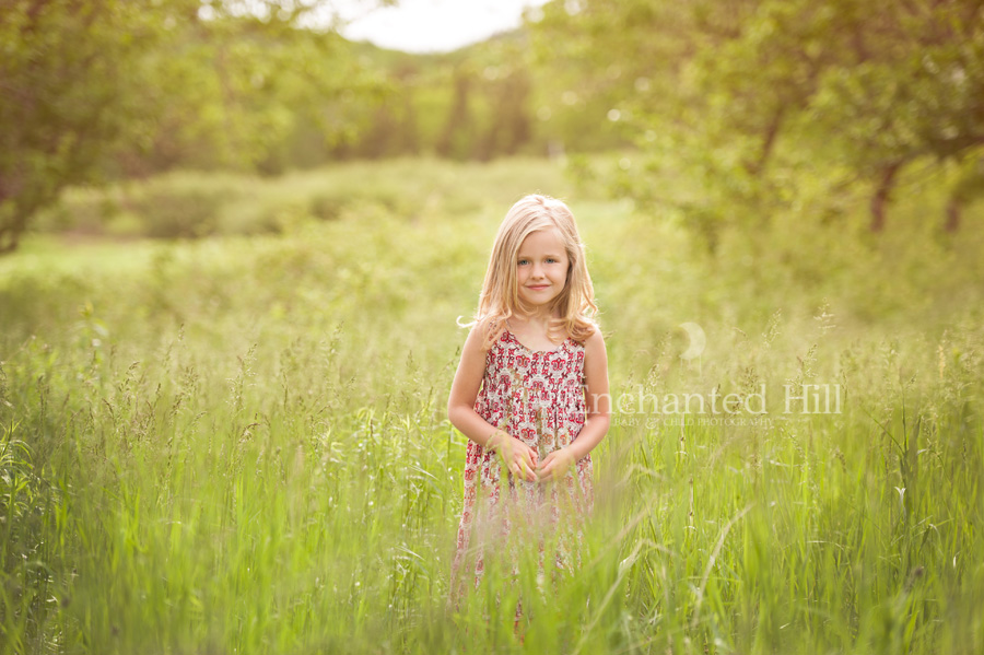 a beautiful girl who is five years old standing in a field of tall grass wearing a red printed dress