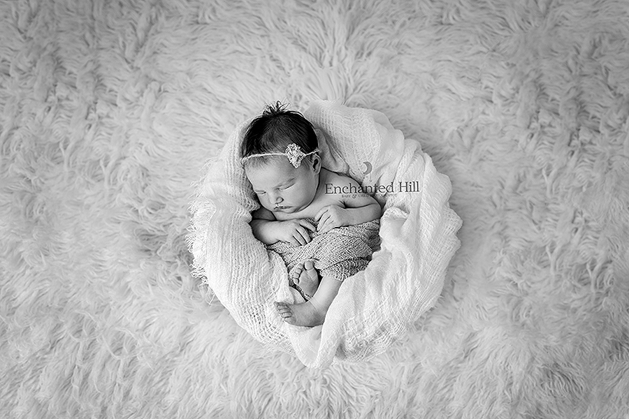 Black and white image of a newborn sleeping in a basket on a  fur rug