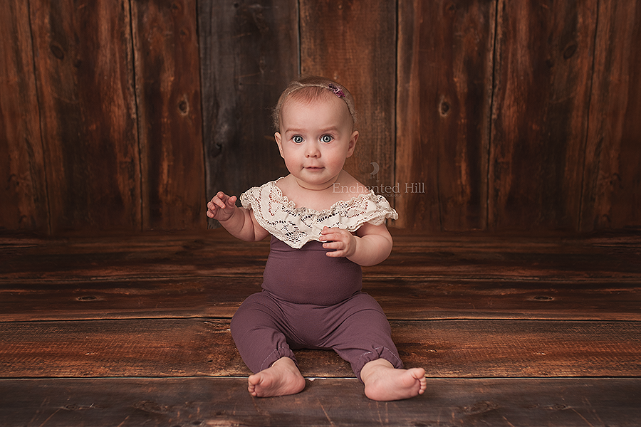 a picture of a baby sitting up wearing a purple romper