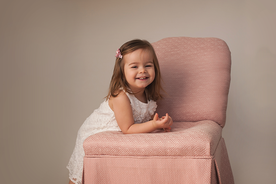 little girl smiling and leaning over pink chair