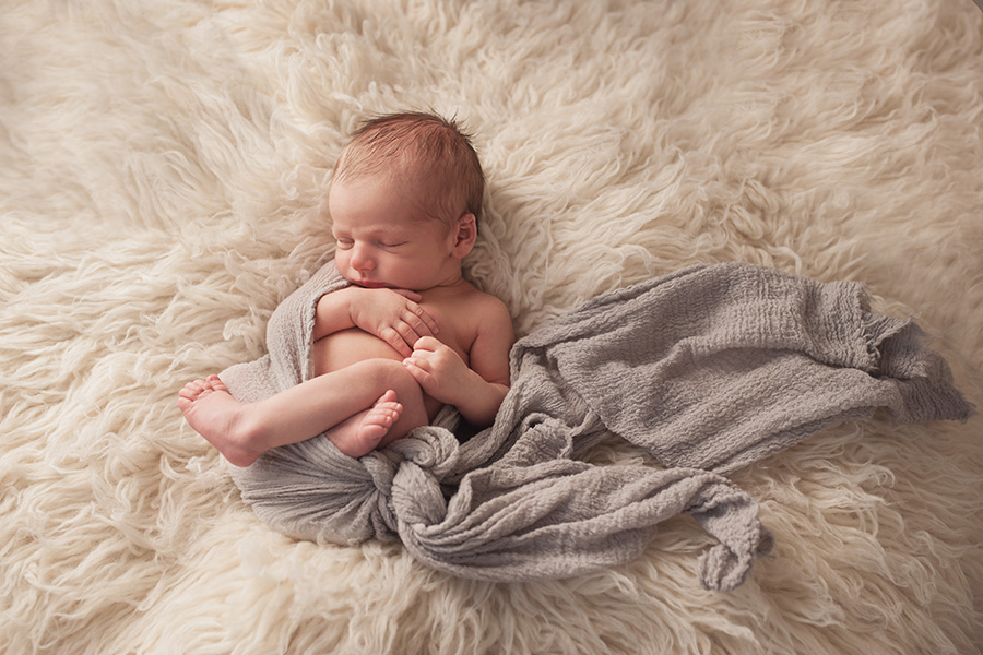 baby laying on cream rug with blue wrap