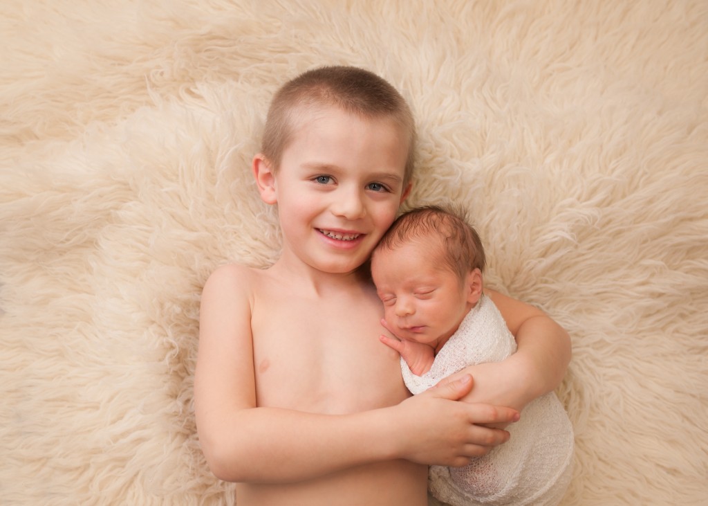 Saint John Photographer baby brother cuddled by his big brother laying on a rug