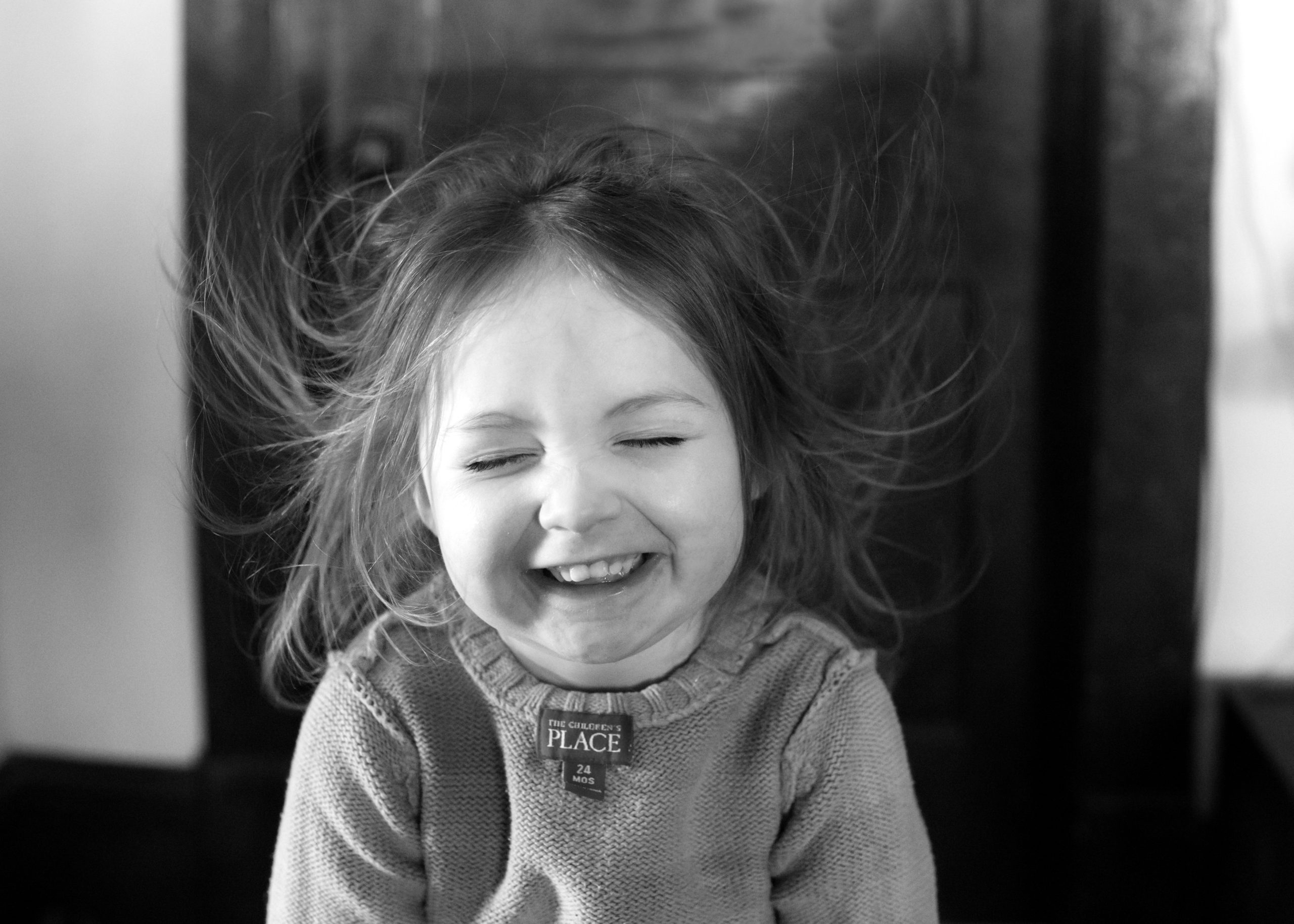 black and white image of a girl laughing while wind blows here hair -Quispamsis Photographer