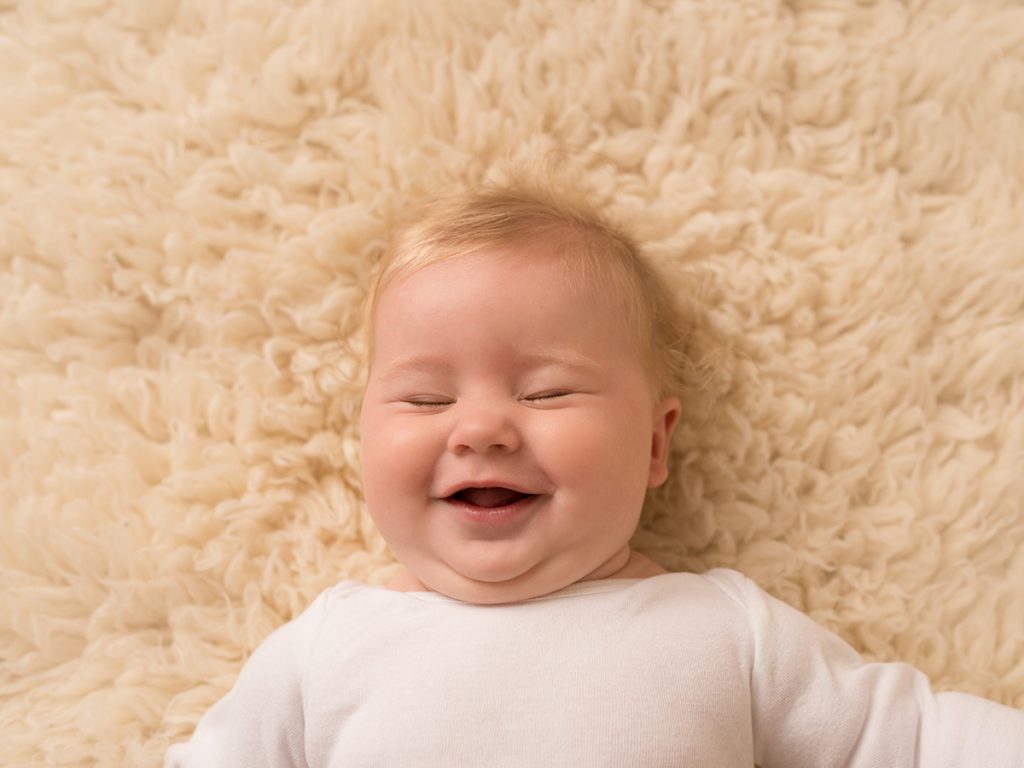 Baby with closed eyes laughing laying on cream rug | Saint John Baby Photographer