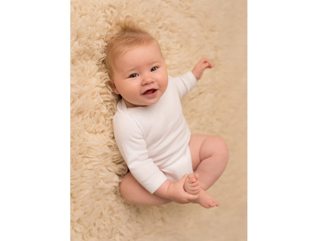 Baby wearing white shirt laying on rug and holding foot with hand | Saint John Baby Photographer