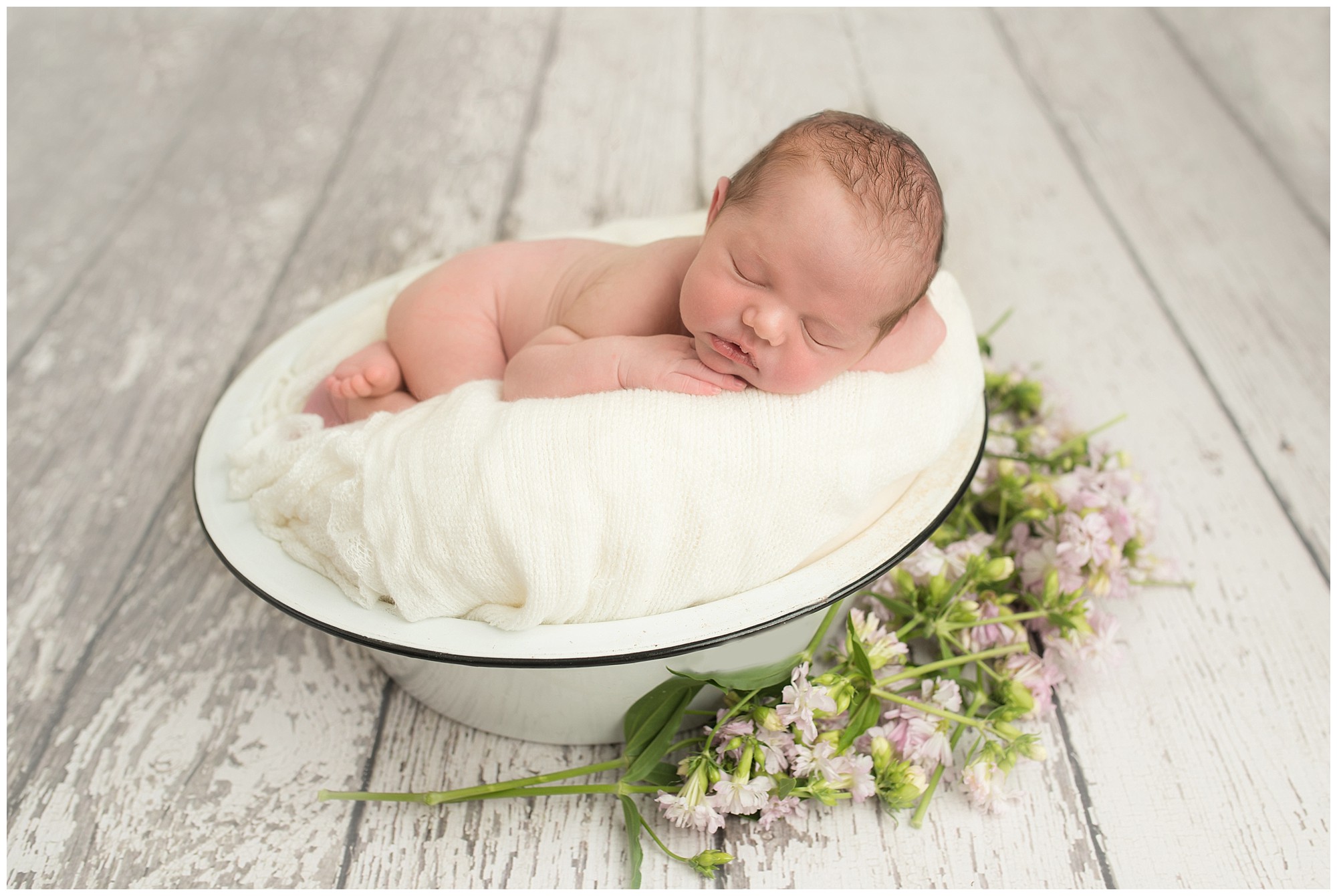 baby laying on a white blanket and flowers