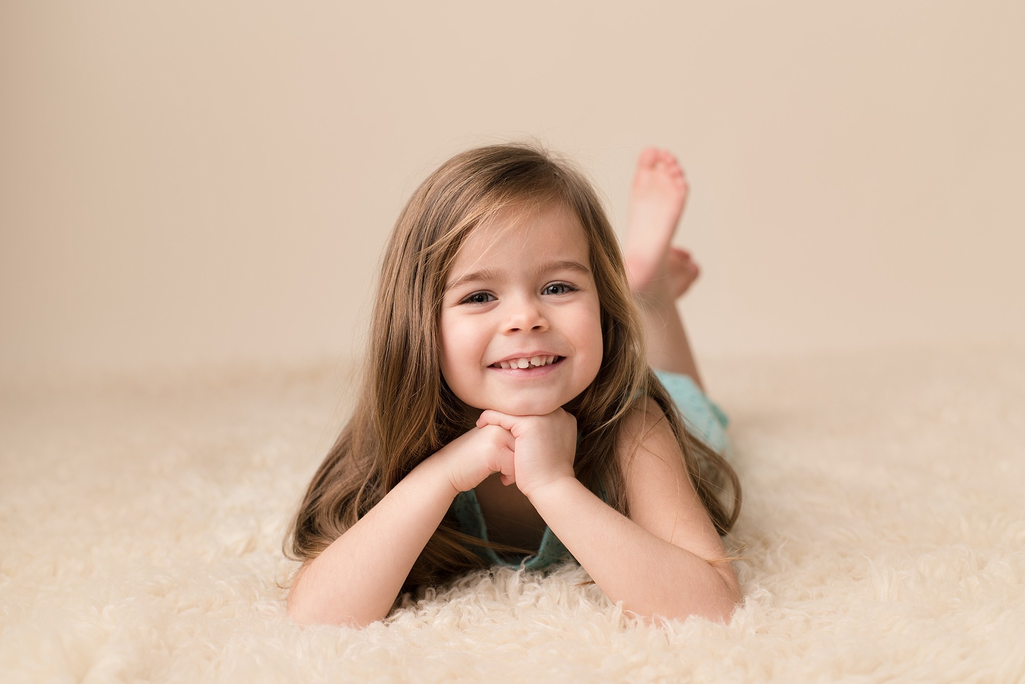 little girl lays on a rug facing the camera with her chin resting on her hands