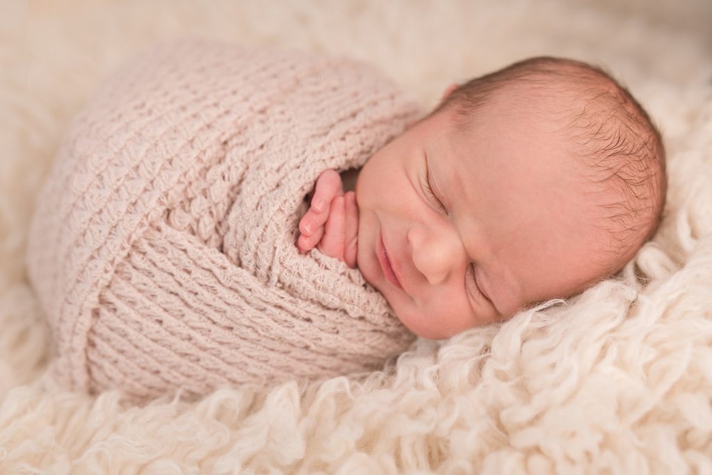 sleeping newborn baby smiling and wrapped in a scarf