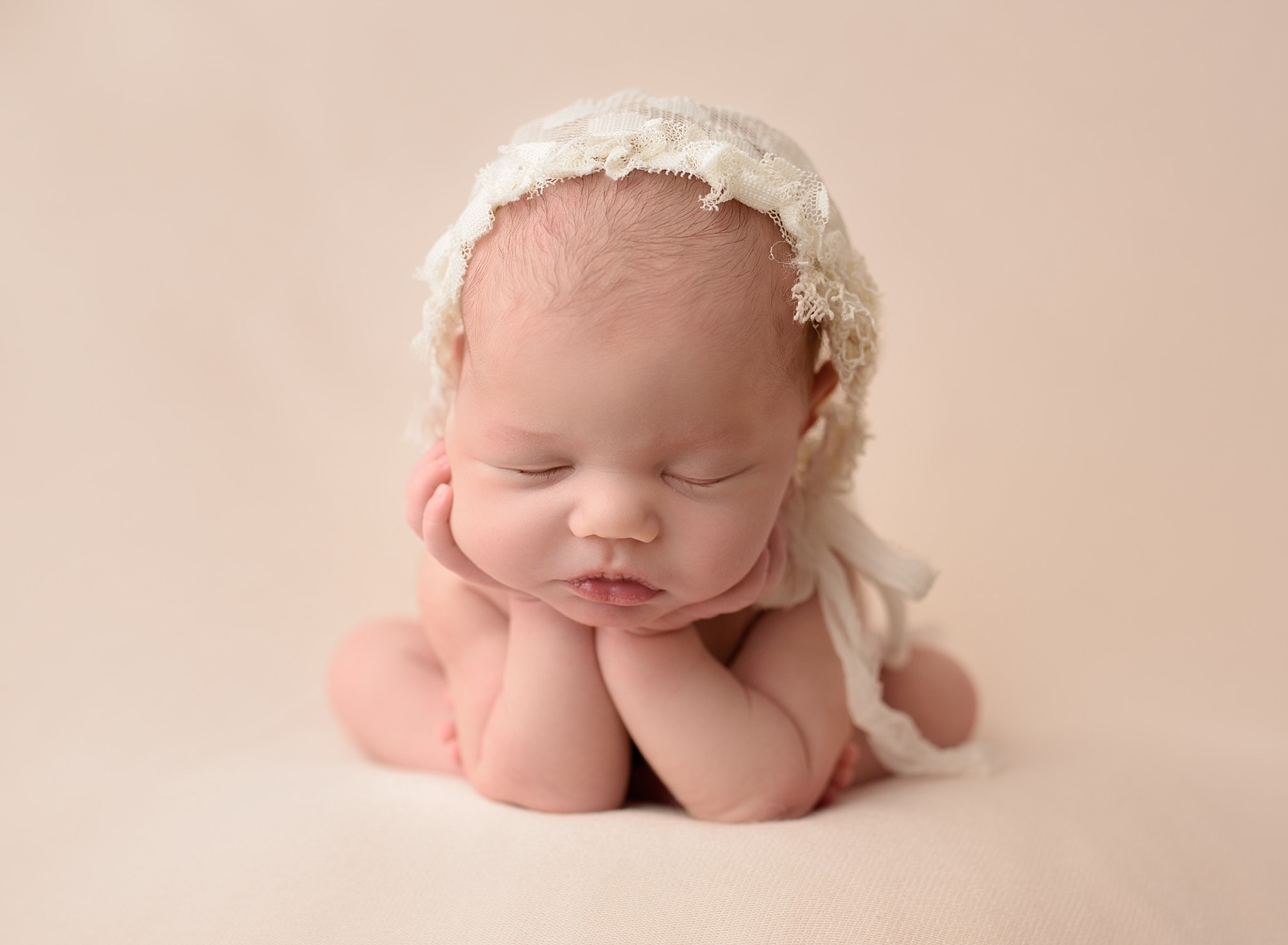newborn baby from quispamsis on blush pink and wearing a lacy bonnet