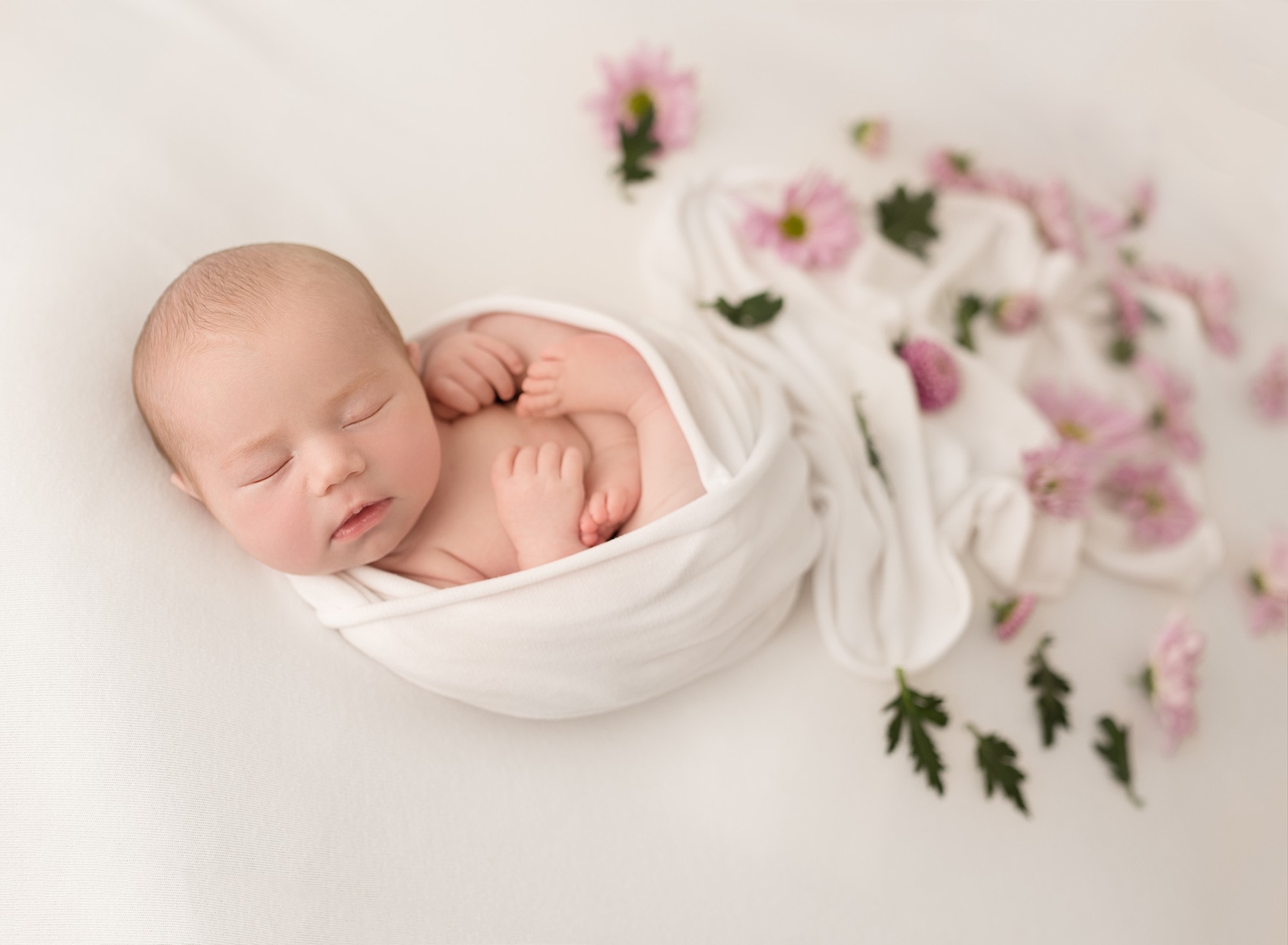 newborn girl wrapped in a scarf with floral around her