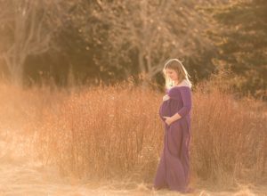 a pregnant mom in the grass wearing a purple gown