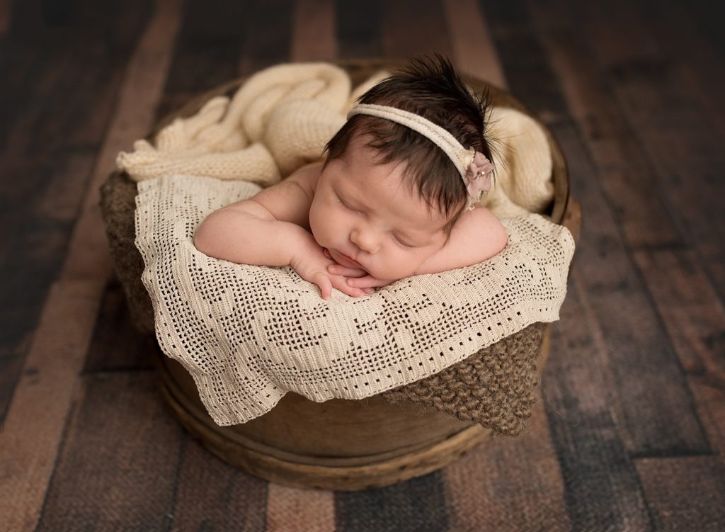 sleeping baby sleeping in a wooden vintage bucket wearing a cream headband