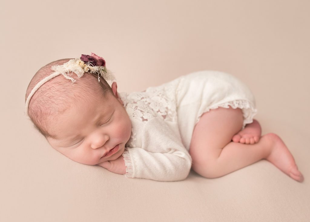 newborn baby wear a white outfit and sleeping on a pink blanket on her tummy