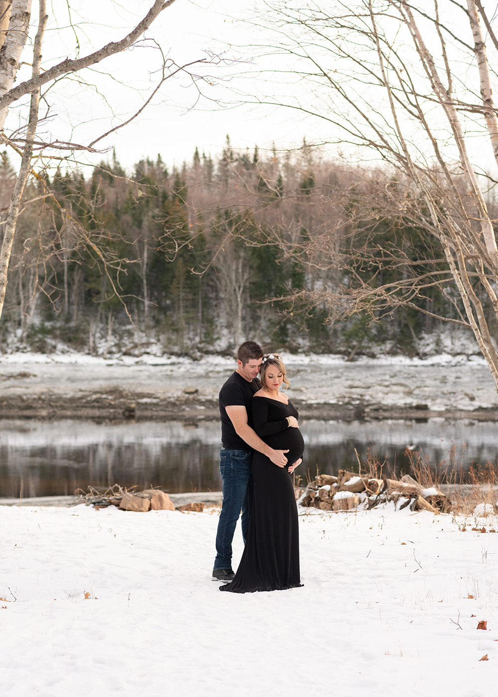 couple cuddled together by the water for pregnancy photos