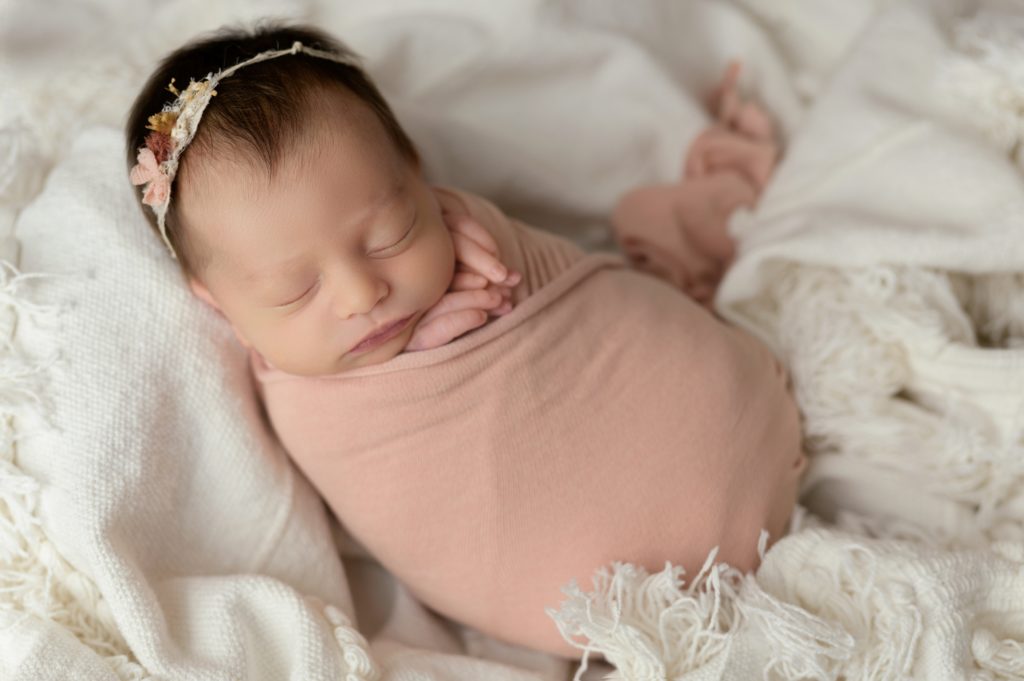 a baby swaddled to help a newborn sleep wearing a floral headband