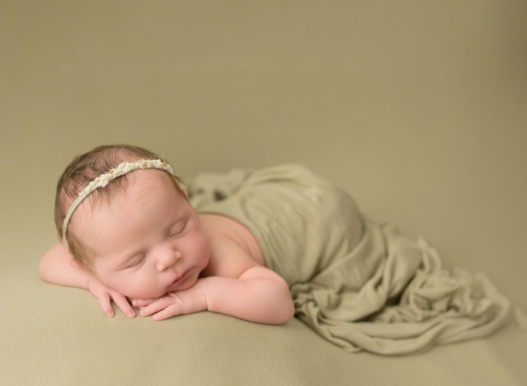 a baby girls is posed on a green blanket with her hands under her chin. The photographer used their favorite lens for newborn photography, a sigma art 50mm