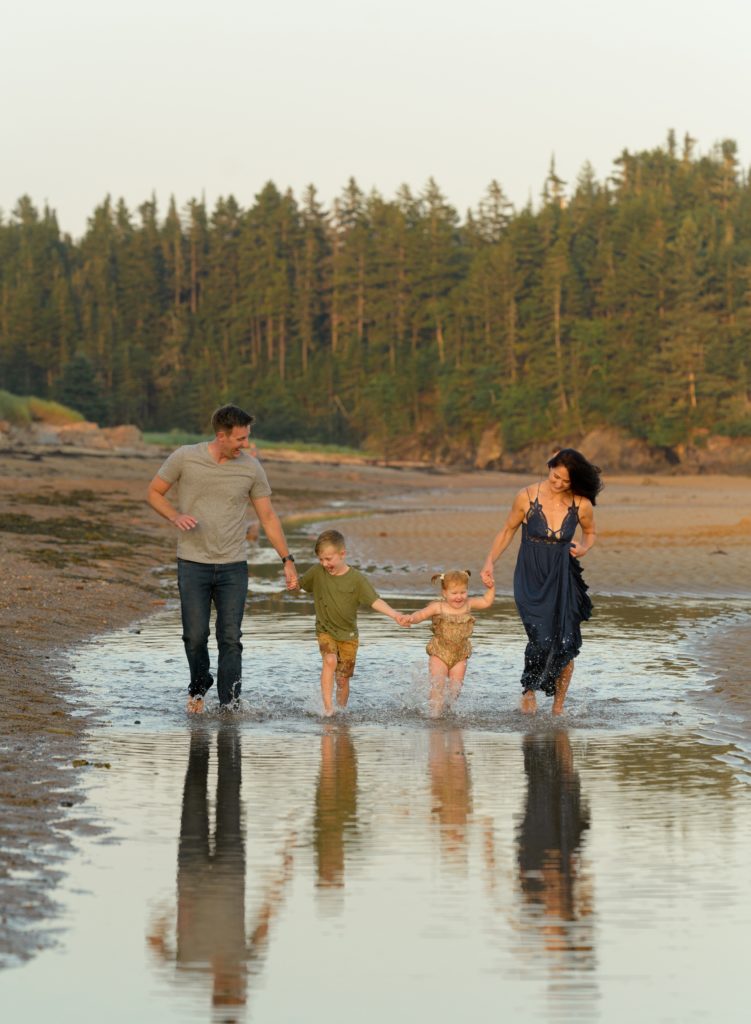 a family is holding hands and running through some shallow water at New River Beach