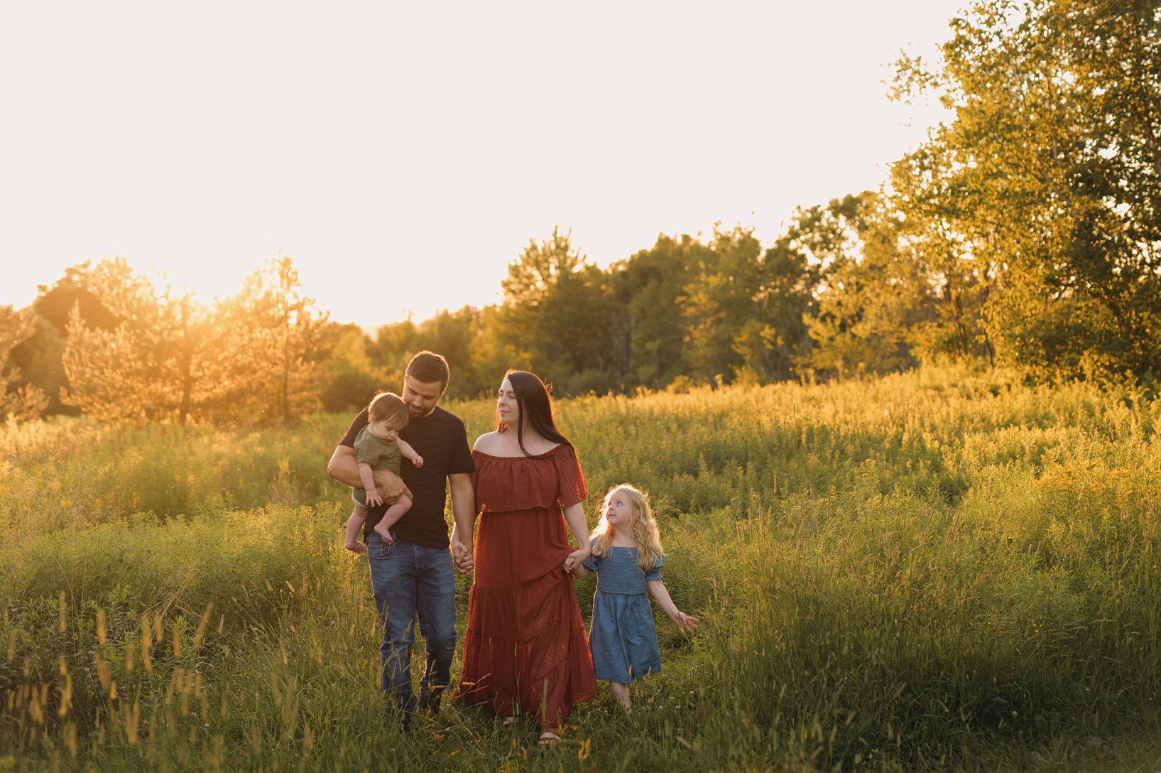 a family is walking through a field at sunset in coordinating clothes