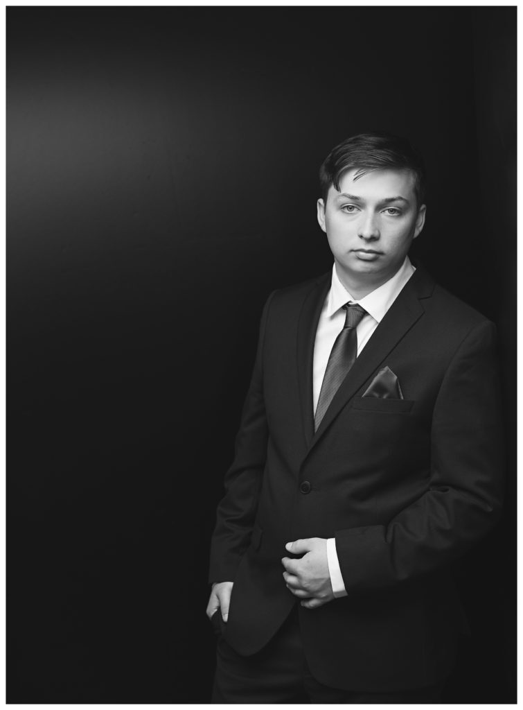 A modern black and white portrait of a teenager who is wearing a suit for his graduation. 