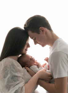 a mom and dad are backlit in the light and holding a new baby between them.